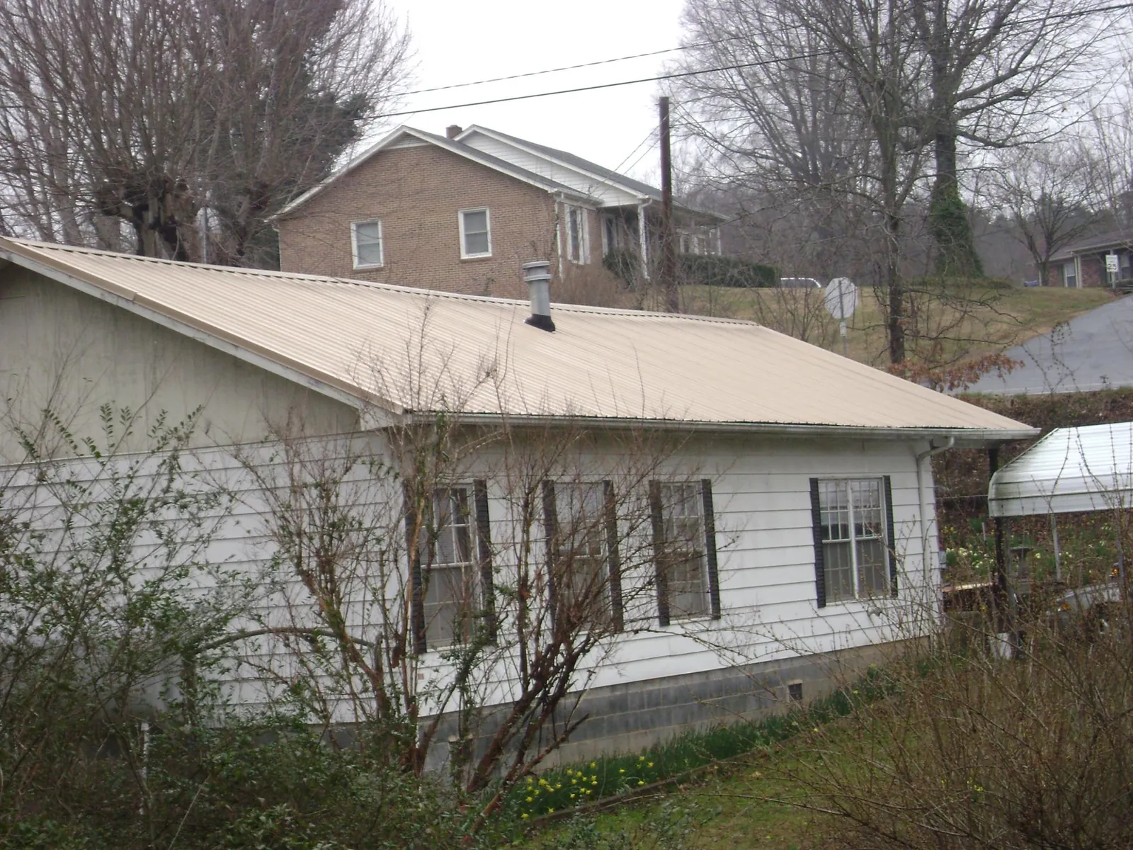 Tan metal roof on a white sided house set into a hillside — Commercial Roofing by Roofing Brothers in Smithville