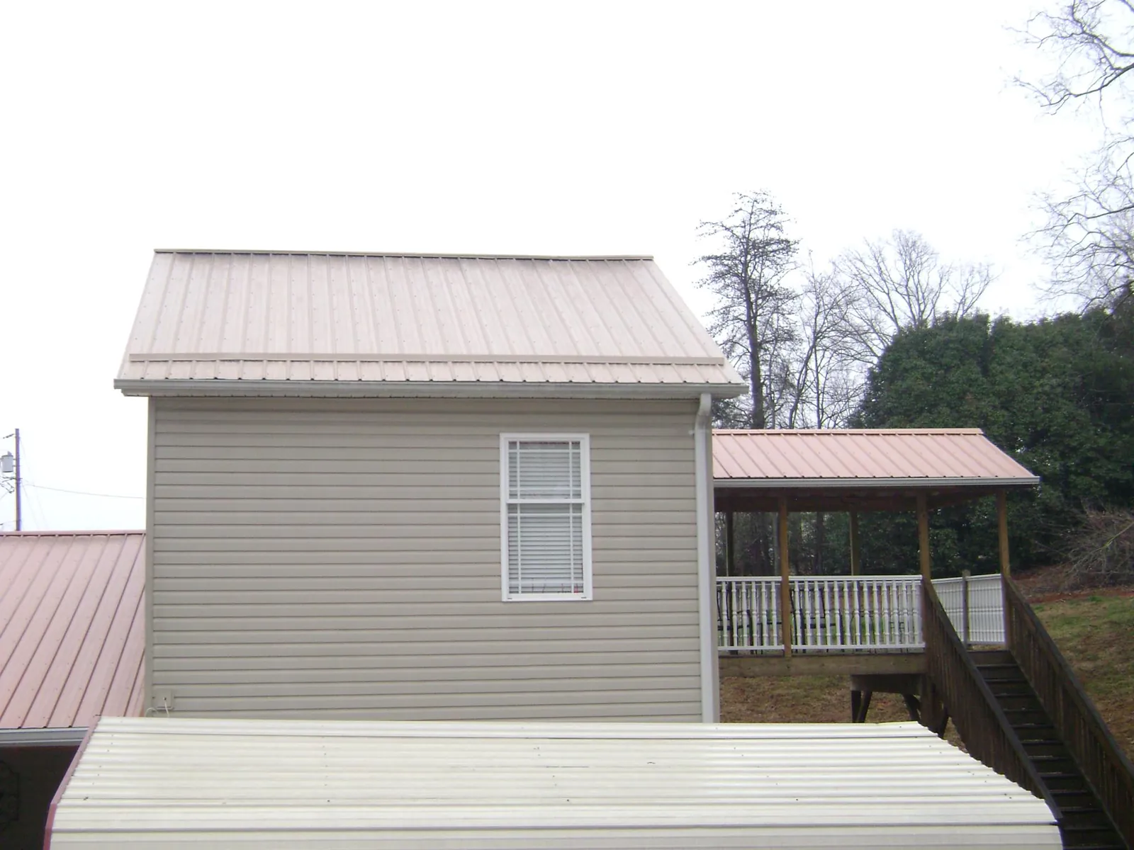 Tan metal roofs on a two story addition and attached porch, from a Roof Replacement job in Smithville